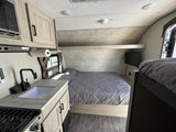 Inside this modern RV rental, find a compact kitchen with microwave, sink, and stovetop, plus a queen bed and bunk.