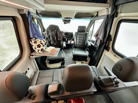 Inside a spacious RV rental, showing swiveling front seats, rear bench, and small workstation.