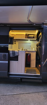 Well-lit rv rental camper van interior with kitchen, microwave, cozy seating/bed, and extended awning, ready for adventure.