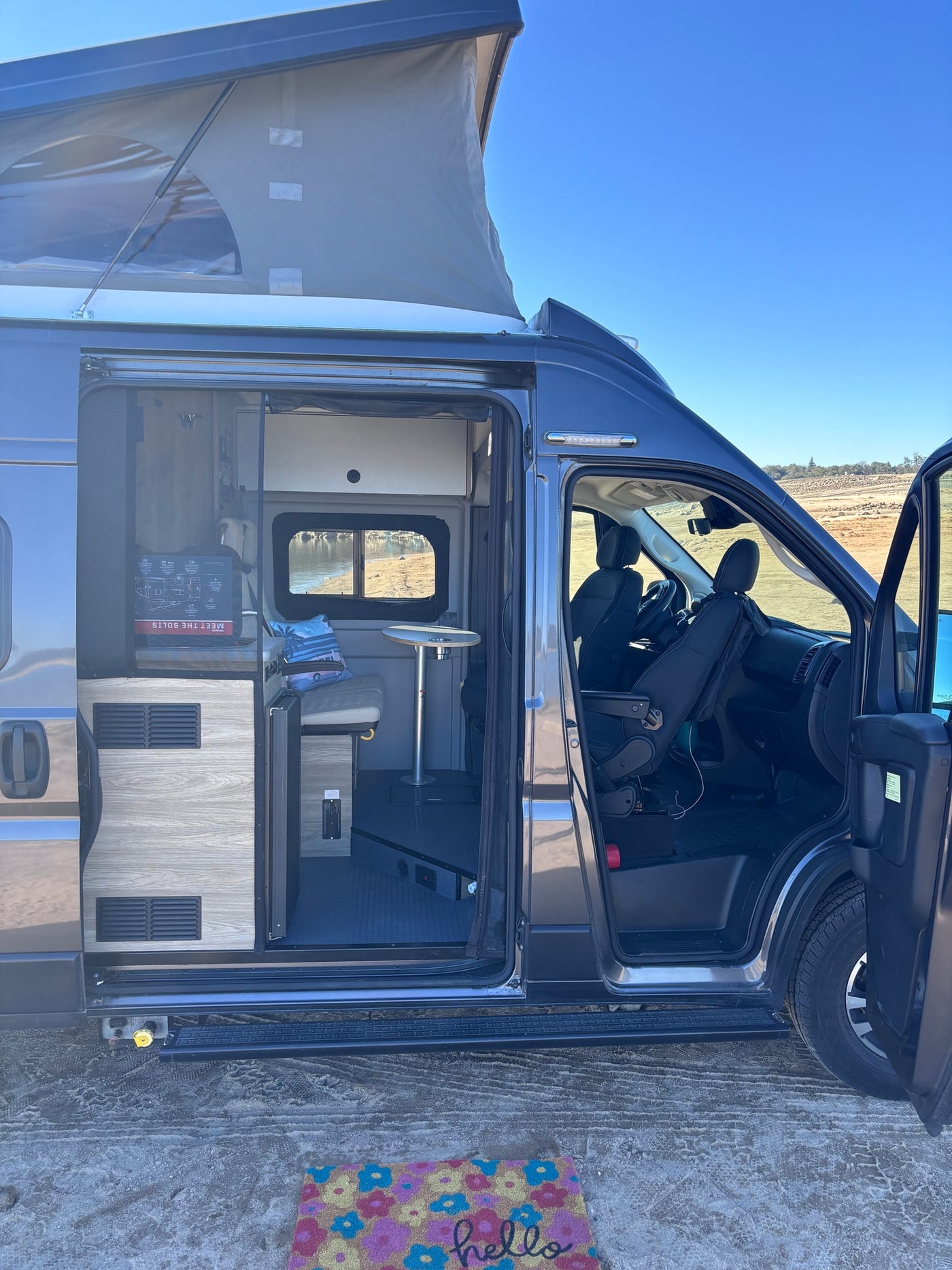 Explore inside this gray pop-top camper van RV rental! Side door open, showing inviting interior & outdoor scenery. — photo 7