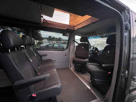 RV rental interior featuring black seating, a driver's area, and an open pop-top roof for light.