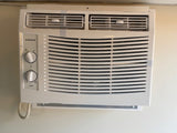 White Amana compact AC unit with control knobs, installed for cooling comfort in this RV rental.