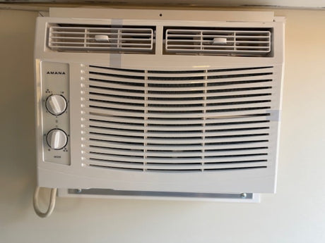 White Amana compact AC unit with control knobs, installed for cooling comfort in this RV rental.
