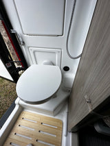Inside a modern RV rental, a compact wet bath with toilet, shower, and wooden floor grates offers practical comfort.