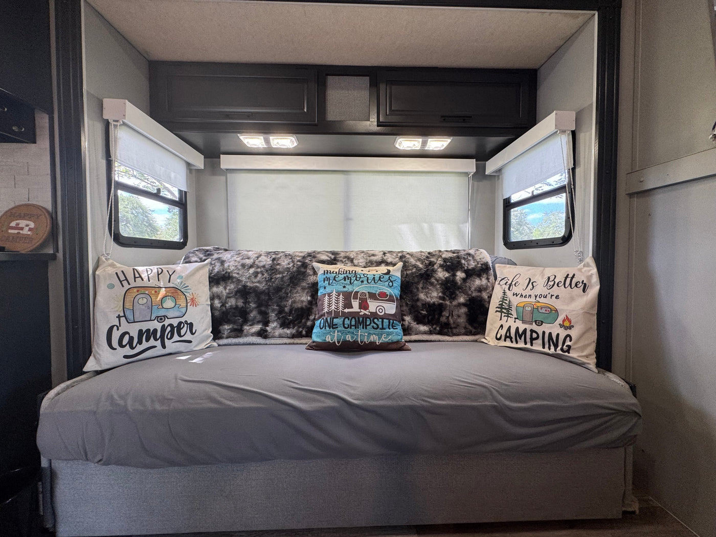 Inside an rv rental: a comfy bed with three camping pillows, a cozy blanket, and windows showcasing greenery outside. — photo 6