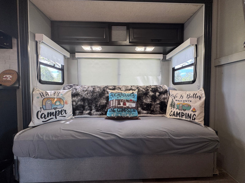 Inside an rv rental: a comfy bed with three camping pillows, a cozy blanket, and windows showcasing greenery outside. — photo 6
