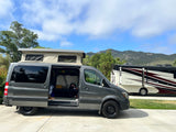 Grey Sprinter camper van with pop-top next to an RV, perfect for your next RV rental adventure in the mountains.