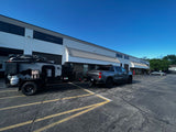 Grey pickup towing a Free Spirit off-road camper with rooftop tent, a unique RV rental, parked outside a business.
