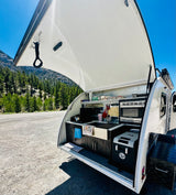 RV rental outdoor kitchen with microwave, sink, and cooler, showcasing mountain and forest scenery.