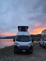 An RV rental and truck camper enjoy a vibrant lake sunset. Serene outdoor camping by the water, perfect for a van life trip.