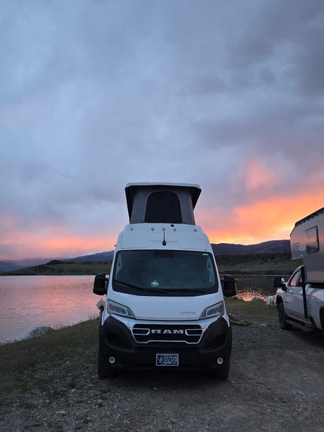 An RV rental and truck camper enjoy a vibrant lake sunset. Serene outdoor camping by the water, perfect for a van life trip.