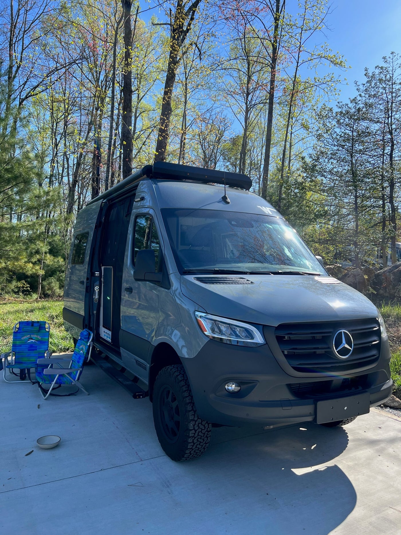 Grey Mercedes Sprinter RV rental camper van parked with open door, chairs, and fresh spring trees in a sunny outdoor setting. — photo 2