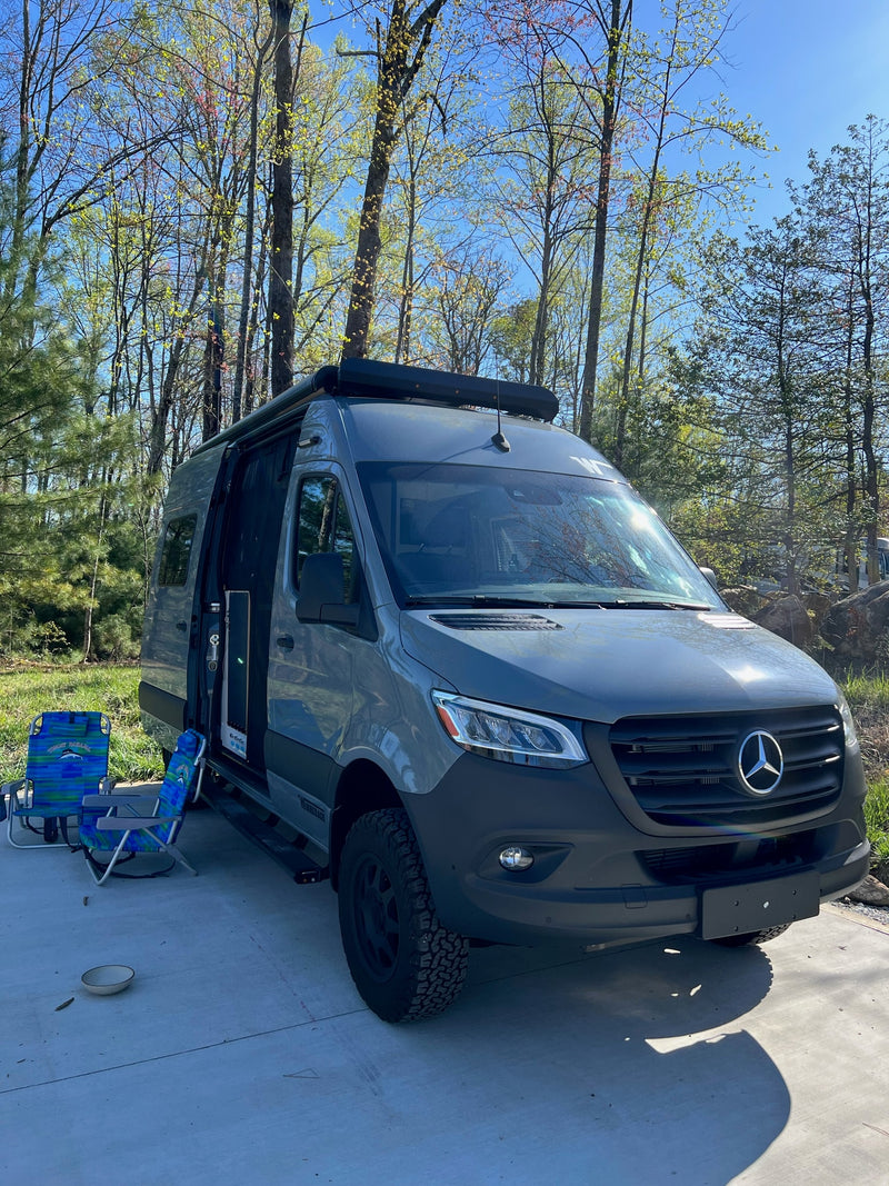 Grey Mercedes Sprinter RV rental camper van parked with open door, chairs, and fresh spring trees in a sunny outdoor setting. — photo 2