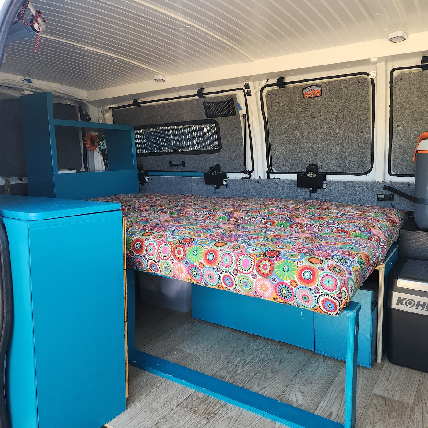 Colorful custom RV rental interior with a vibrant bed, blue cabinetry, and storage solutions for comfortable travel. — photo 13
