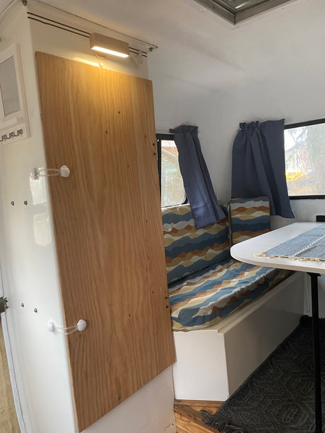 Interior of an rv rental: a light wood partition, patterned bench seating, dining table, and curtained windows create a cozy space.