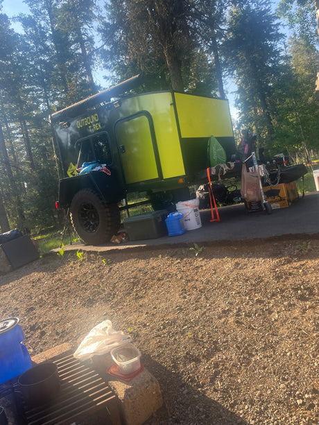 This vibrant Outbound T-Rex off-road camper trailer, ready for adventure, offers an RV rental experience at a campsite.