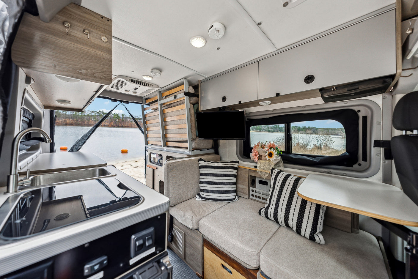 Spacious RV rental interior with kitchen, modular seating/bed, TV, and beautiful lake view from the open rear.