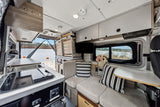Spacious RV rental interior with kitchen, modular seating/bed, TV, and beautiful lake view from the open rear.