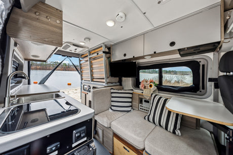 Spacious RV rental interior with kitchen, modular seating/bed, TV, and beautiful lake view from the open rear.