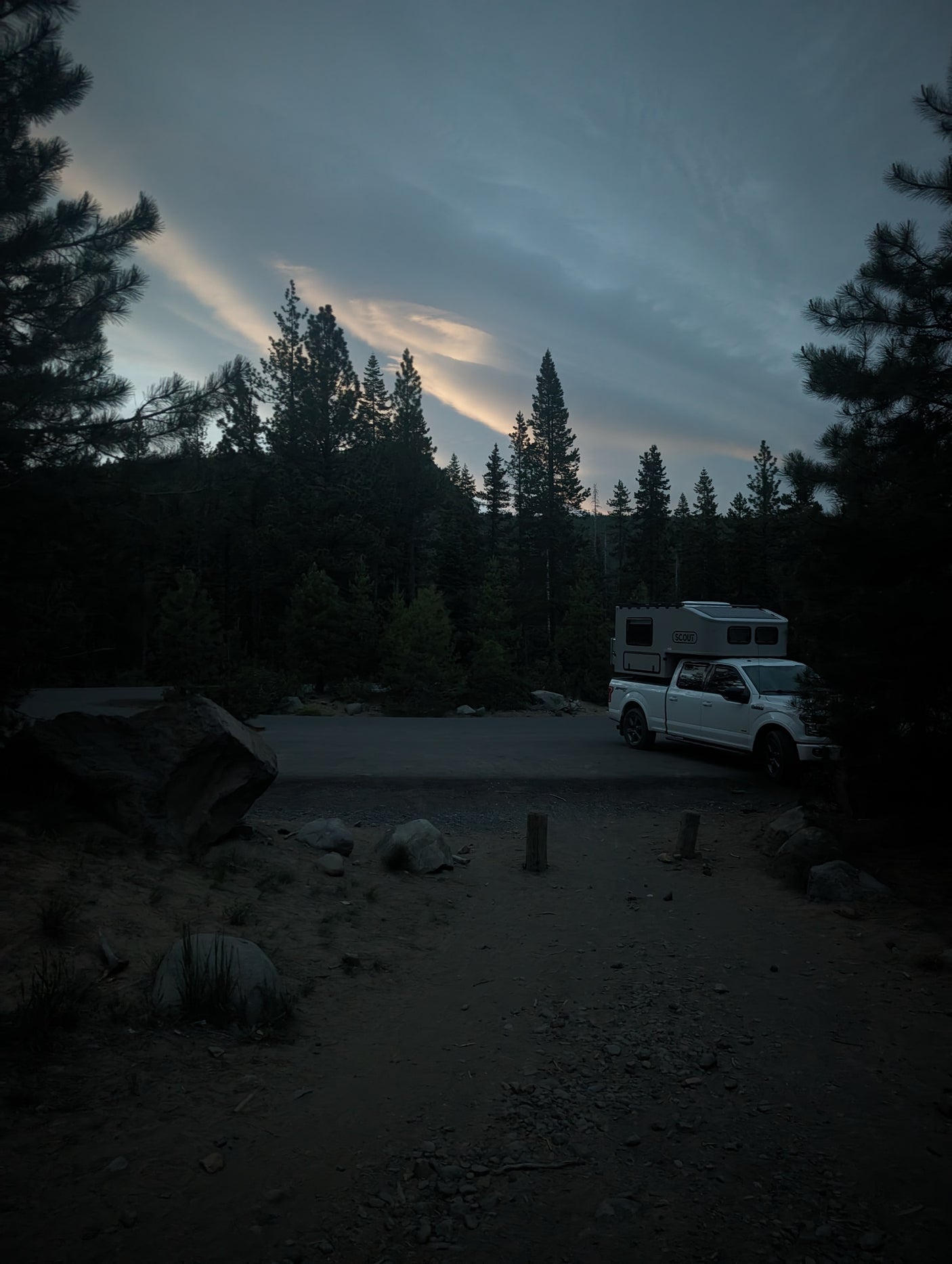 White truck with camper at a dark forest campsite at dusk. Your perfect RV rental for exploring the wilderness.