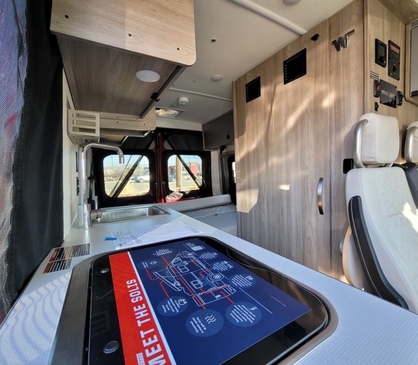  offering scenic views of a forest campground from pop-top windows.|Cozy pop-top **rv rental** camper bed with blue sleeping bag and orange pillows