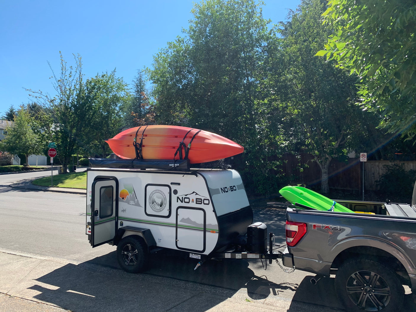 RV rental set up for adventure: A compact "No Boundaries" travel trailer with kayaks hitched to a pickup truck on a sunny day.