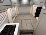Compact rv rental interior with a cozy, segmented bed, induction cooktop, and ample overhead storage.