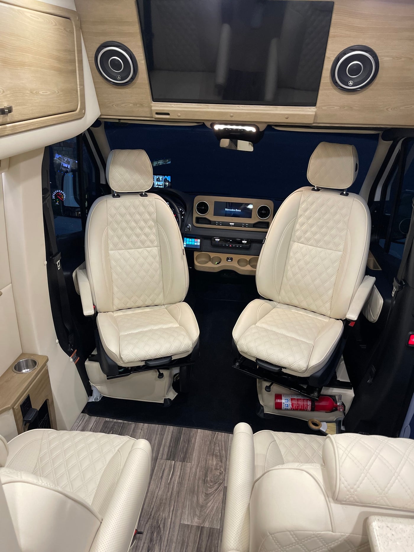Inside a premium **rv rental**: cream quilted seats, wood-accented Mercedes-Benz dashboard, entertainment screen & speakers. — photo 11