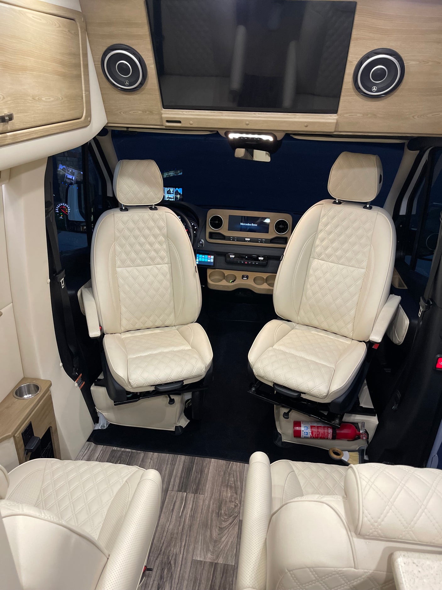 Inside a premium **rv rental**: cream quilted seats, wood-accented Mercedes-Benz dashboard, entertainment screen & speakers.