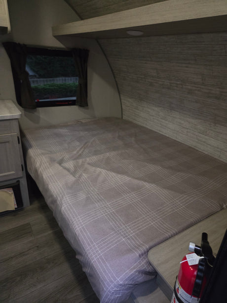 Cozy RV rental bedroom featuring a plaid bed, window with curtains, and a visible fire extinguisher for safety.