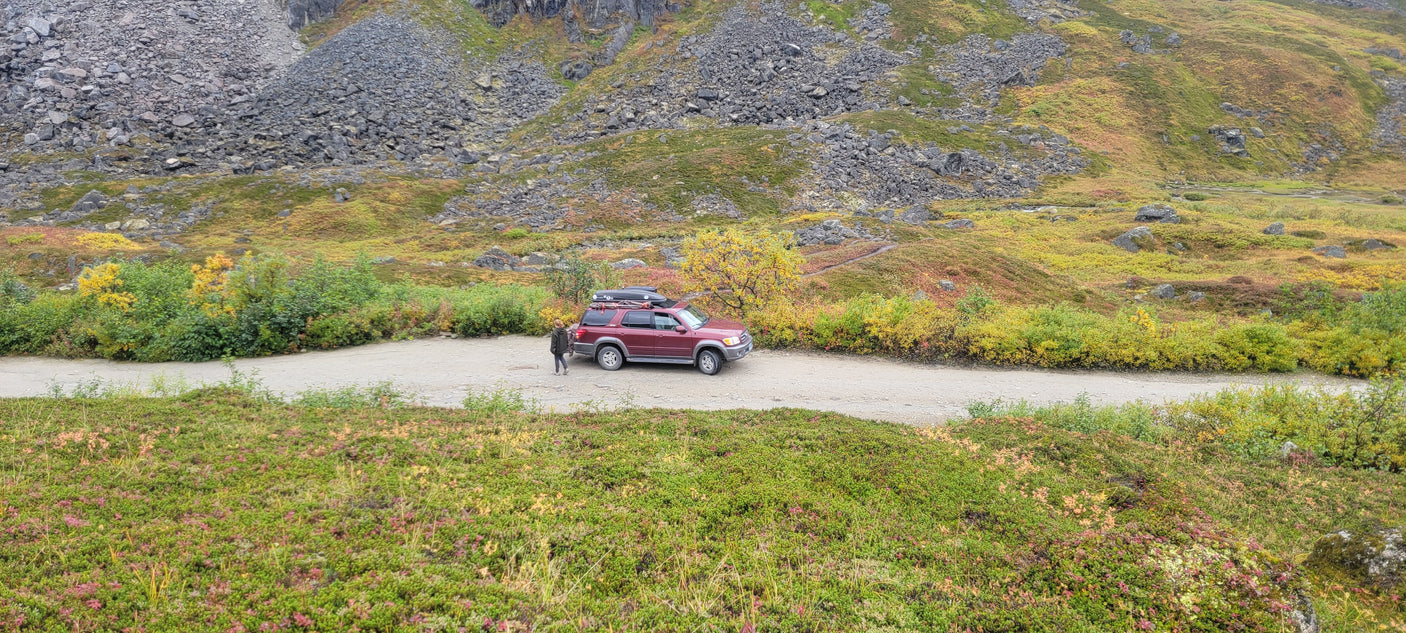 Maroon SUV on a dirt road in fall mountains, great for exploring. Consider an rv rental for similar scenic adventures!