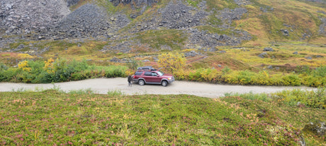 Maroon SUV on a dirt road in fall mountains, great for exploring. Consider an rv rental for similar scenic adventures!