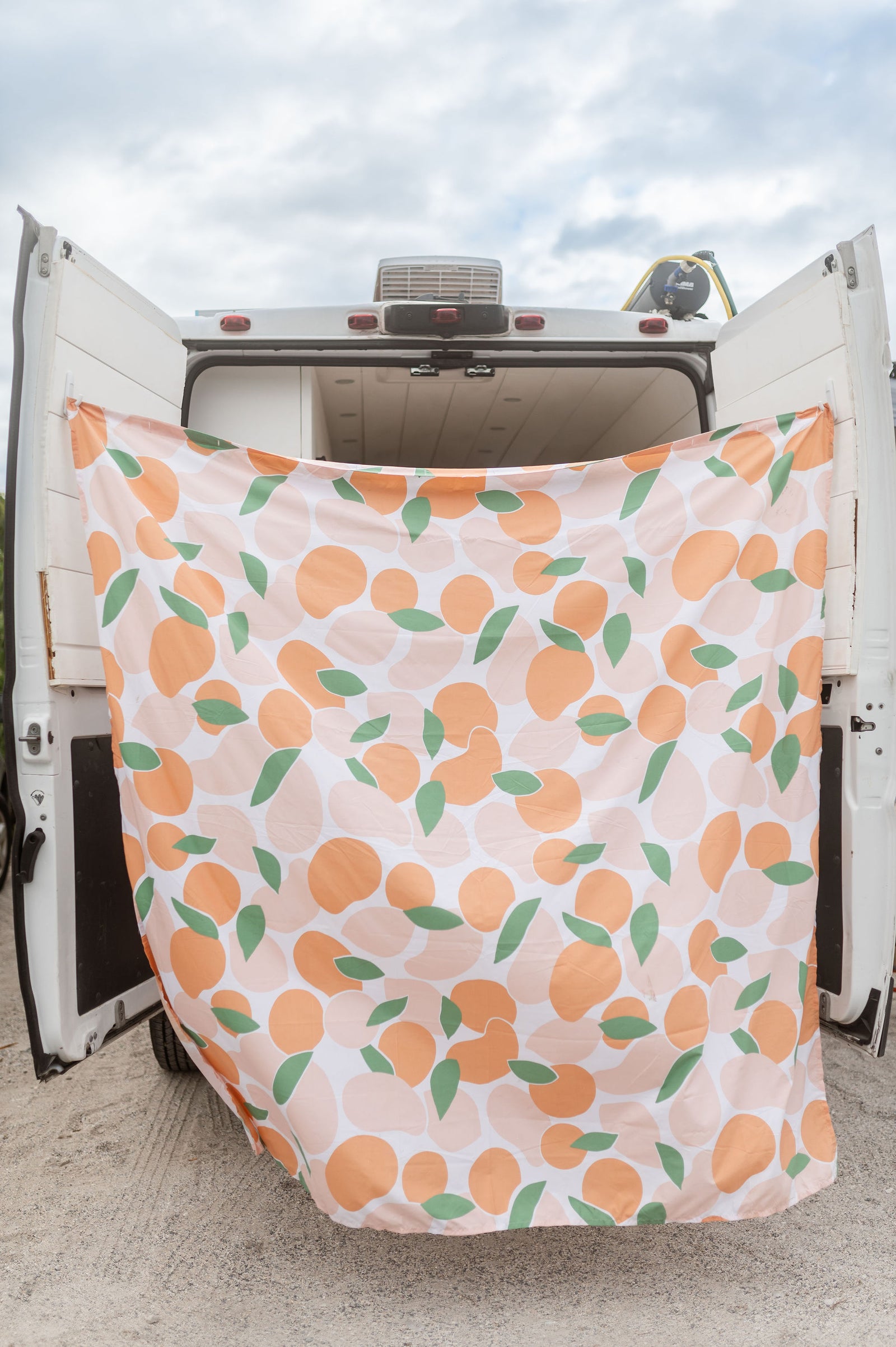 White RV rental with open rear doors. A vibrant peach and leaf patterned curtain hangs, creating a private outdoor space.