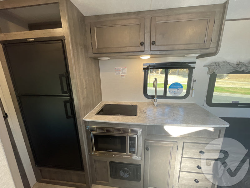 RV rental kitchen area featuring a Dometic fridge, stovetop, microwave, sink, and ample cabinet storage. — photo 11