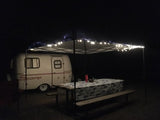 Cozy night camping with a small travel trailer rental, lit canopy, and picnic table at a campsite.