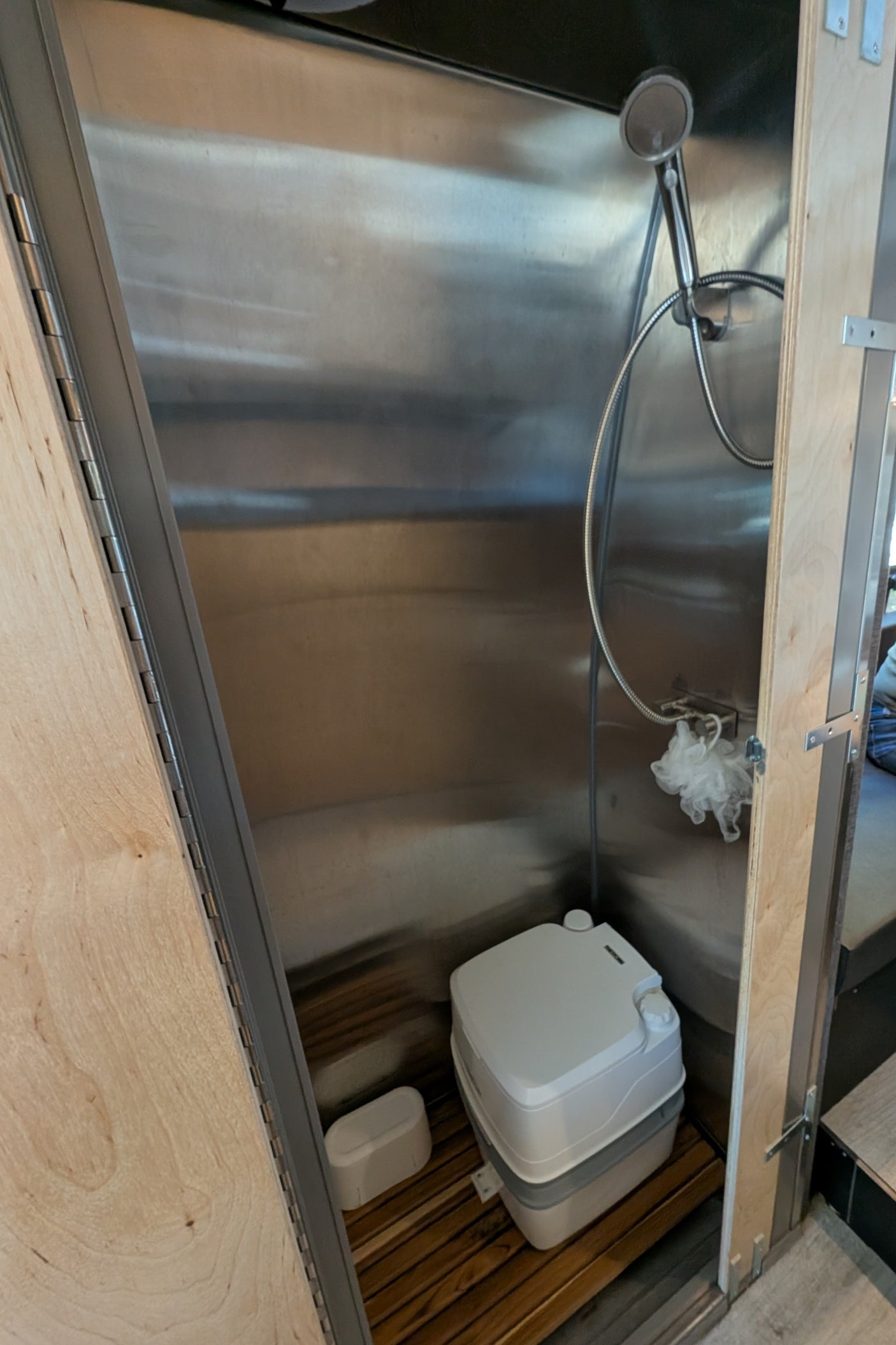 RV rental: space-saving shower and portable toilet in a stainless steel enclosure with a wood slat floor, ideal for van life.