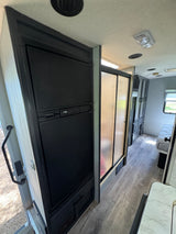 RV rental interior with a black refrigerator, frosted shower stall, wood-look floor, and rear bedroom.