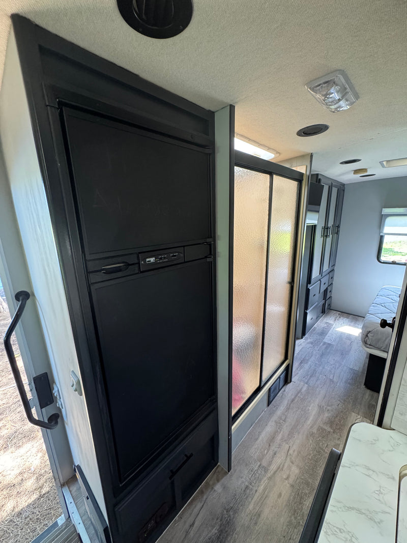 RV rental interior with a black refrigerator, frosted shower stall, wood-look floor, and rear bedroom. — photo 10