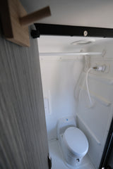 Compact white RV bathroom with a toilet, shower hose, and small wall panel. Ideal for an rv rental.