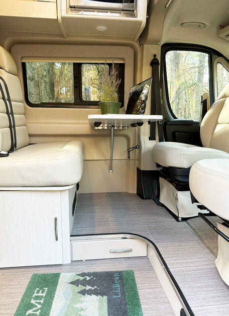 Inside this modern rv rental: light seating, wood-look cabinets, a table for work, and panoramic nature views. Spacious and bright.