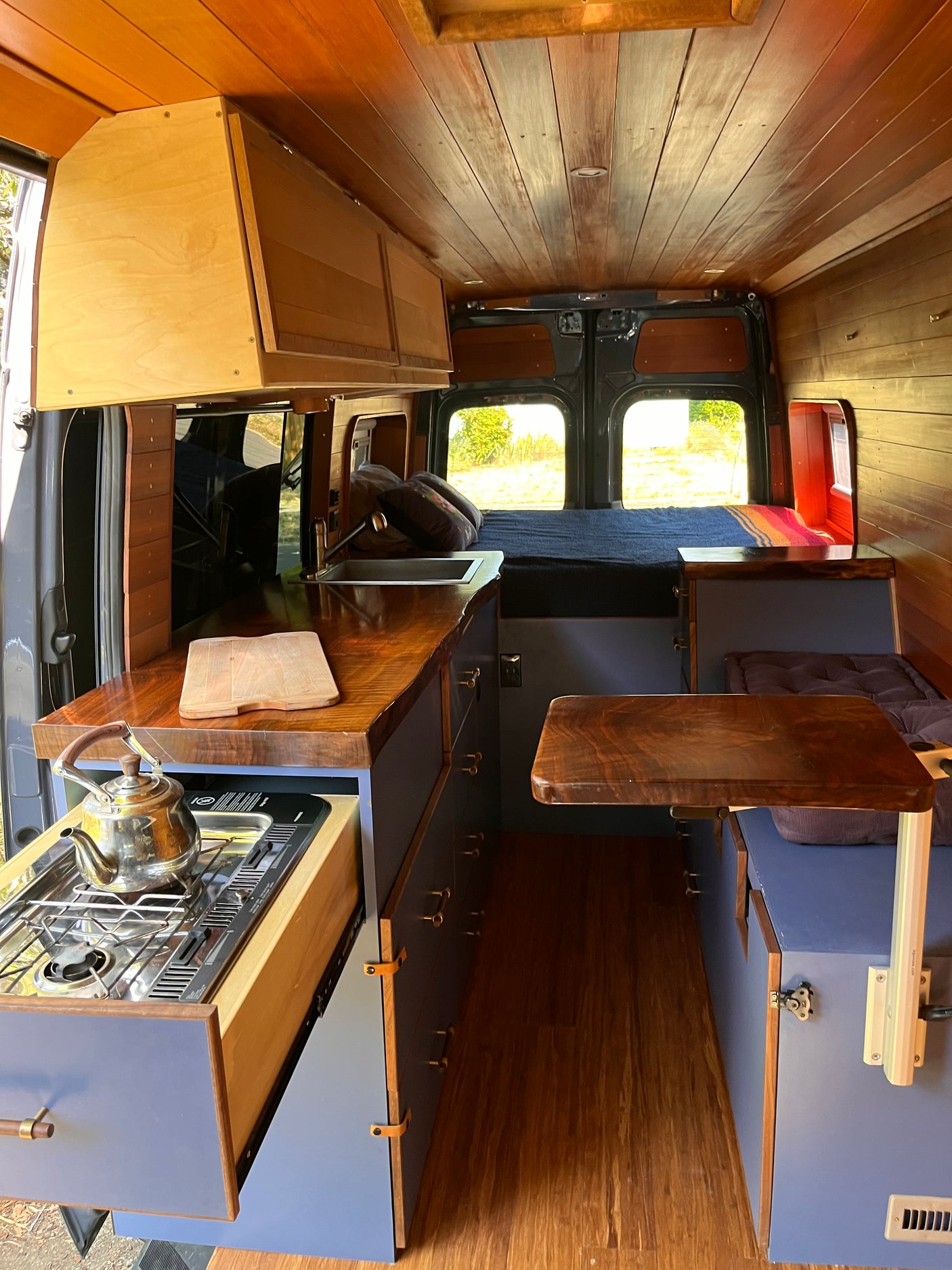 RV rental: Inside a custom wood-paneled camper van featuring a compact kitchen, comfortable bed, and storage.
