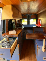 RV rental: Inside a custom wood-paneled camper van featuring a compact kitchen, comfortable bed, and storage.