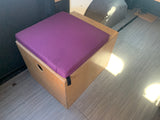 Inside an rv rental: a light wood storage box topped with a bright purple cushion for seating, on a patterned floor.