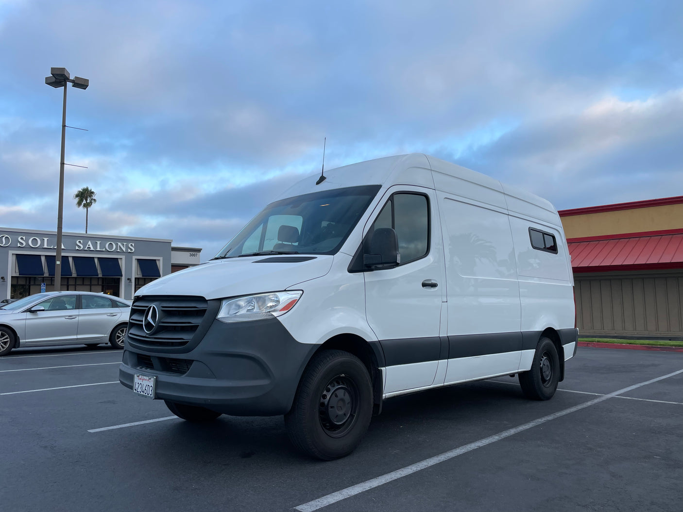 White Mercedes Sprinter van, converted for RV rental, parked in a lot under cloudy skies.