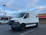 White Mercedes Sprinter van, converted for RV rental, parked in a lot under cloudy skies.