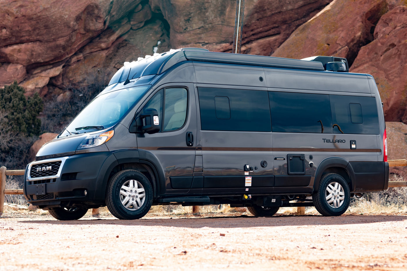  parked on a dirt path with a rocky landscape behind it.|Front view of a dark grey Ram ProMaster camper van RV rental — photo 7