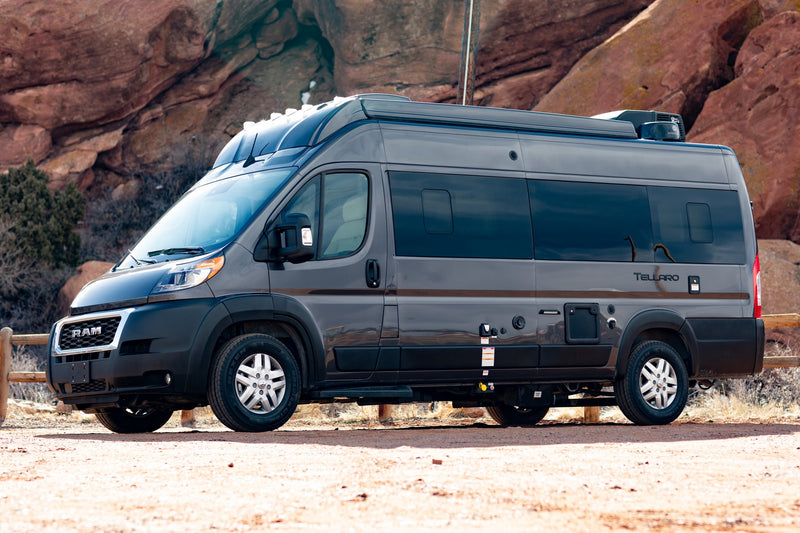  parked on a dirt path with a rocky landscape behind it.|Front view of a dark grey Ram ProMaster camper van RV rental — photo 7