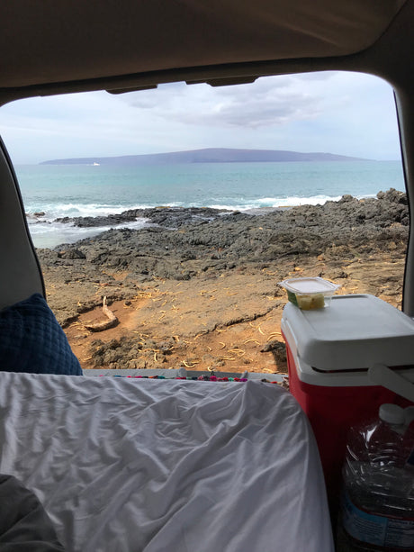RV rental escape: Stunning ocean vista with rocky shore & distant island from a cozy car camping setup.