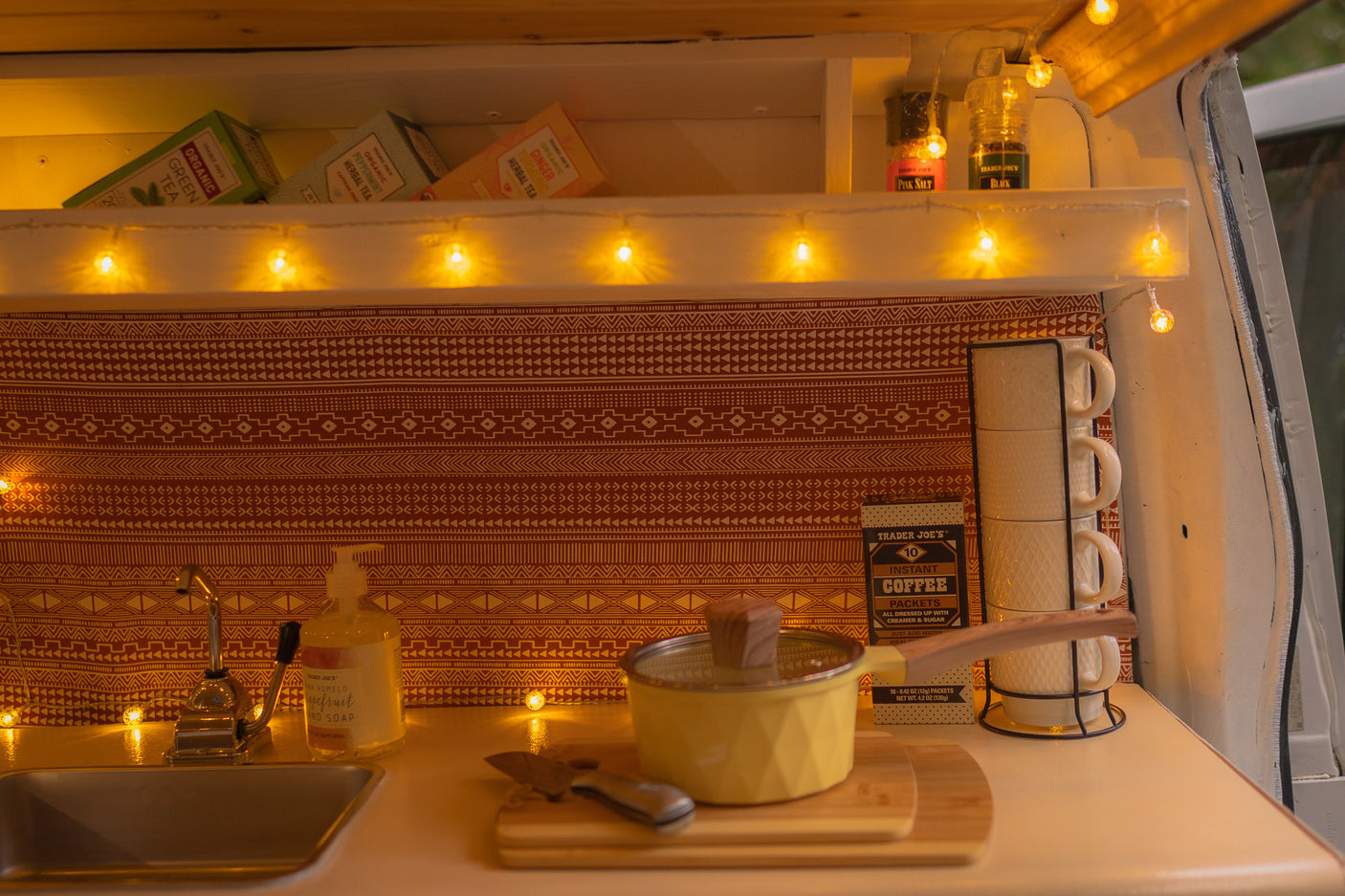 Warmly lit RV rental kitchen featuring Trader Joe's teas, spices, and coffee, a mini sink, and cooking essentials.