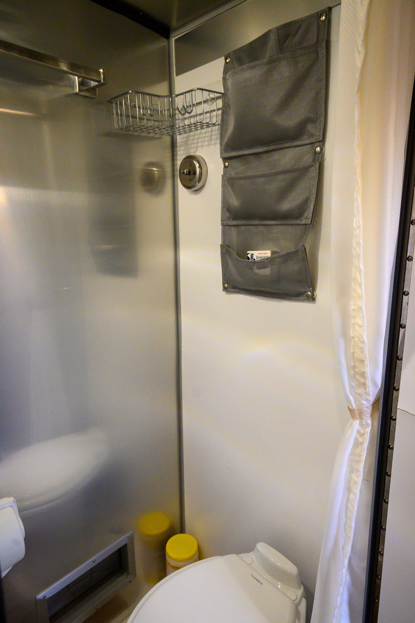 Inside an RV rental, this compact bathroom features a toilet, shower, and wall organizer with Trader Joe's shampoo.